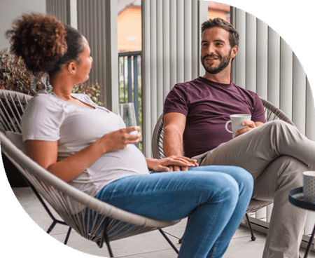 Pregnant wife with husband sitting in chairs drinking coffee