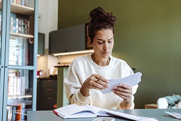 Young woman examines envelopes in her home office as she works on her budget.