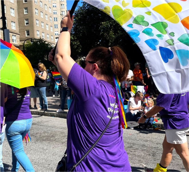 A Pride participant waves a Pride flag with rainbow colored hearts through the streets.