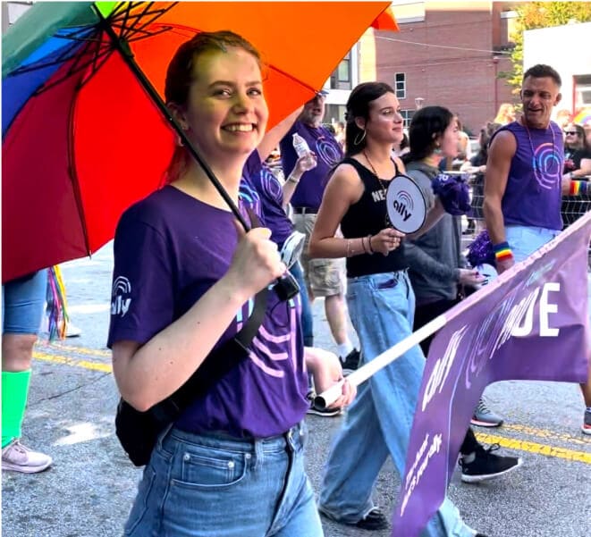 A smiling Pride participant carries a rainbow umbrella in the parade