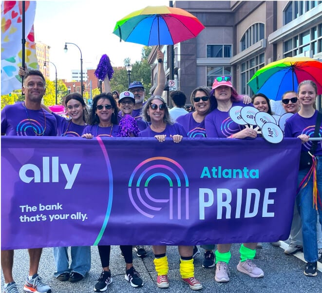 A happy group of people poses with the Ally Atlanta Pride parade banner.