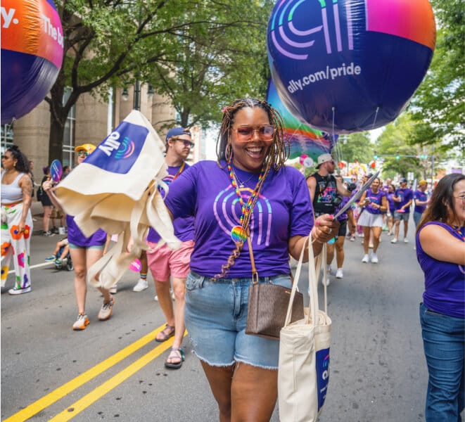 A cheerful Pride participant wearing a purple Ally Pride shirt marches in the parade.