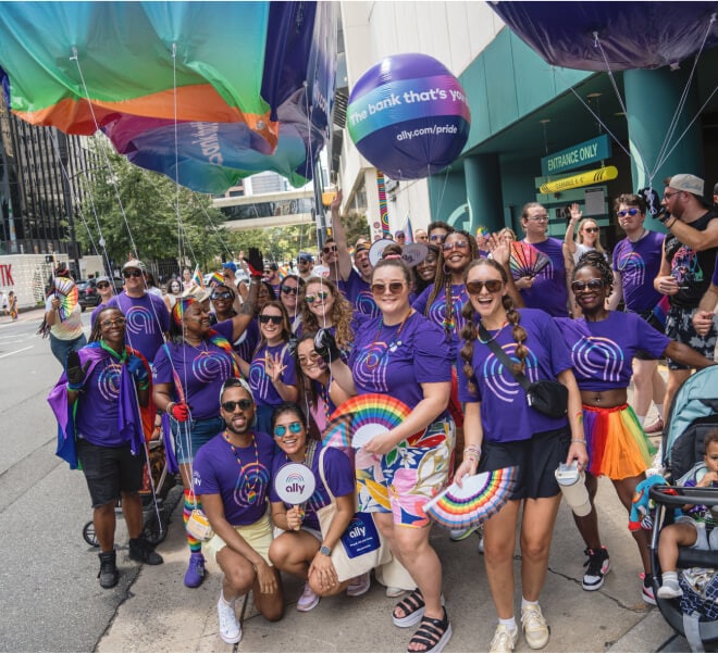 A group of smiling Pride attendees wearing Ally shirts pose together.