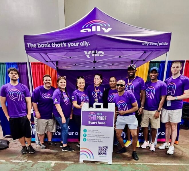 A group of smiling Ally Pride attendees pose together under a purple tent.