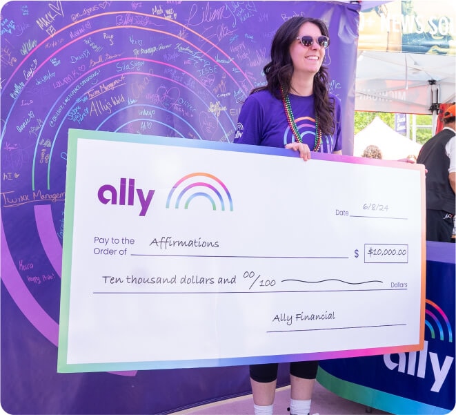 A smiling Ally Pride participant displays a donation check made out to Affirmations.