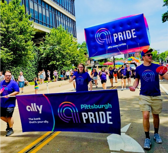 Energetic parade participants carry an Ally Pittsburgh Pride banner and balloon through the streets.