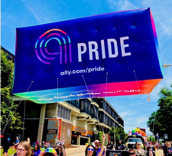 A spirited group of parade participants display a large and colorful Ally Pride balloon.