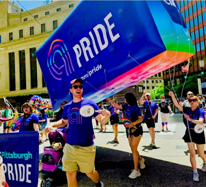 Energetic parade participants carry an Ally Pittsburgh Pride banner and balloon through the streets.