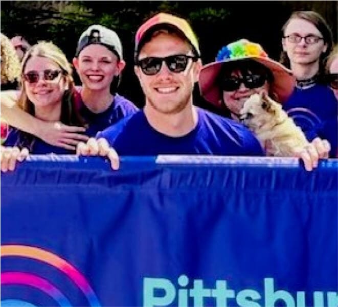 Smiling Pride attendees hold up the Ally Pittsburgh Pride banner.