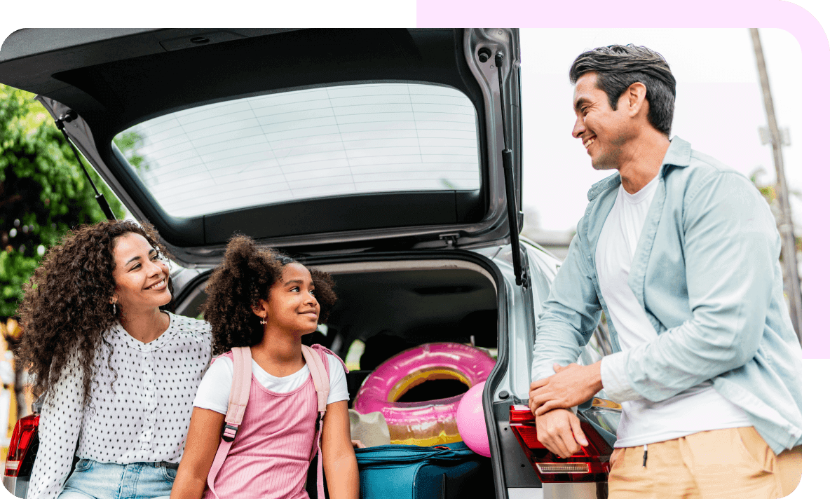 A family smiling next to their packed up car trunk