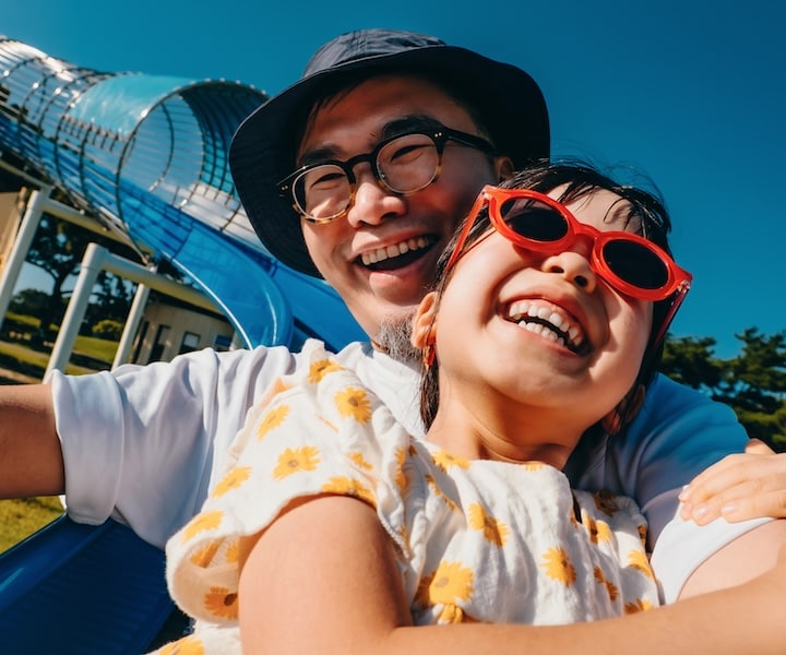 A young father and daughter smiling as they go down a slide together