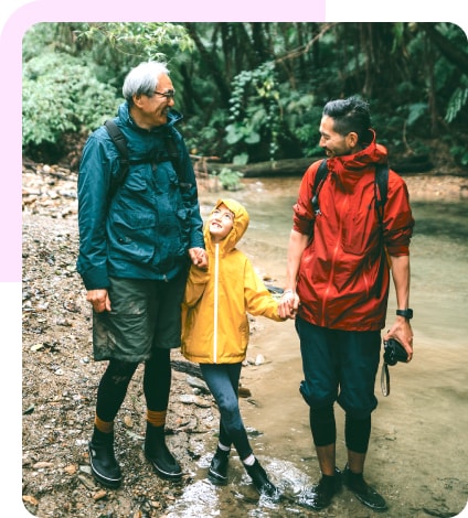 A grandfather, father and daughter holding hands on a hike in a rainforest