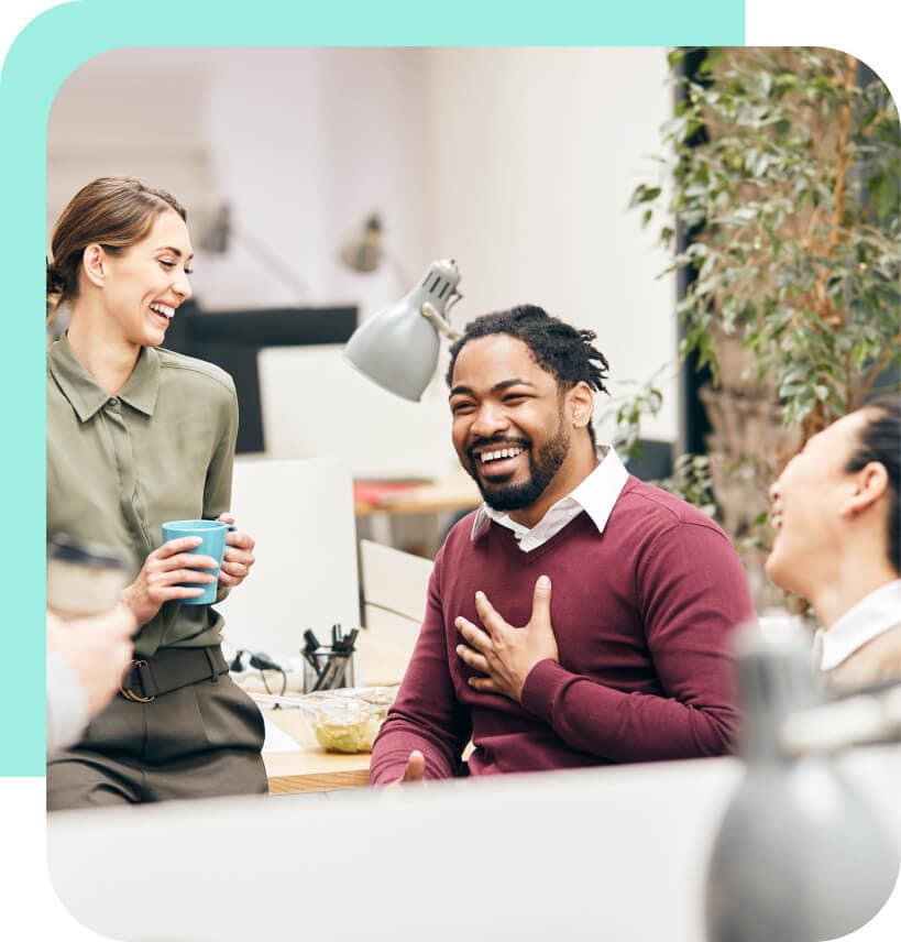 In an office setting, a standing woman laughs with a sitting man and woman.