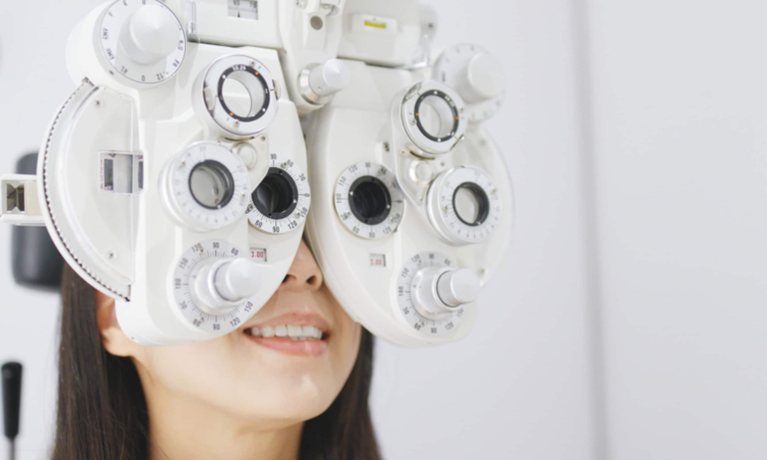 Woman has eyes up to eye doctor lens measuring machine.