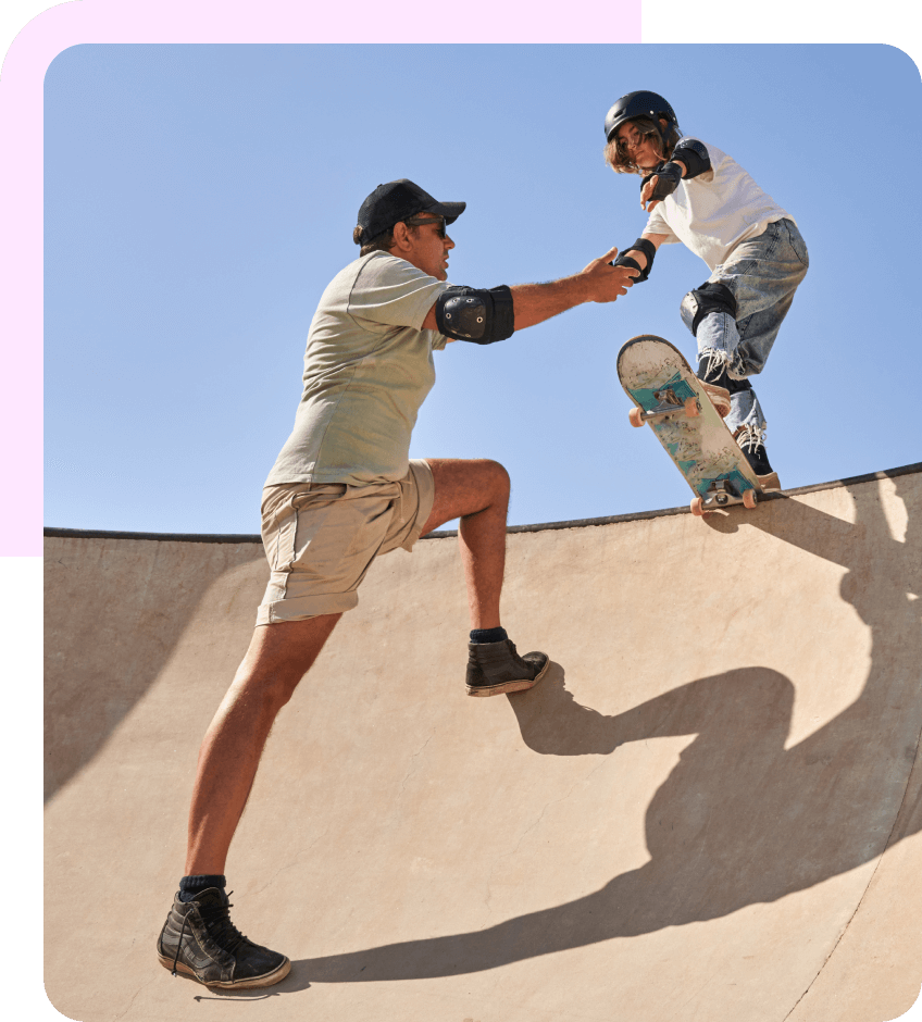 A man supports a kid skateboarding down a ramp by holding his hand