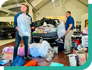 Two Ally volunteers stand in a room holding bags full of clothes, with lots of other bags and boxes full of donations on the floor.