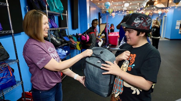 Female Ally employee handing a young boy a backpack