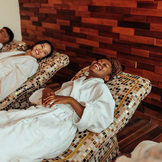 Two cheerful couples are enjoying their day at the spa. They are lying on the spa beds in their bathrobes smiling and talking to each other.