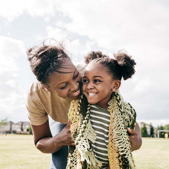 Mom hugging daughter from behind while playing outside