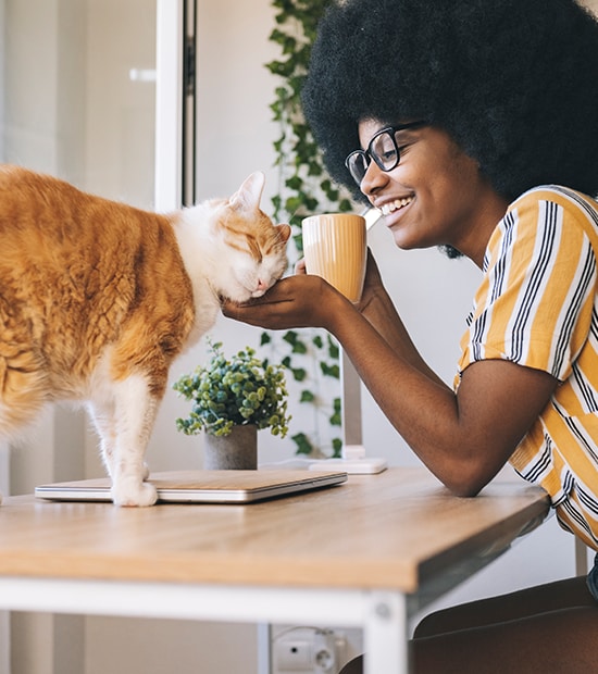  Woman sips her coffee at a table while petting her orange cat