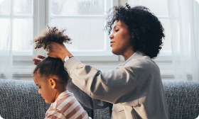 A mother puts her young daughter’s hair up in a ponytail