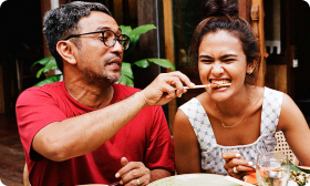 An older man feeds a younger woman food on a stick